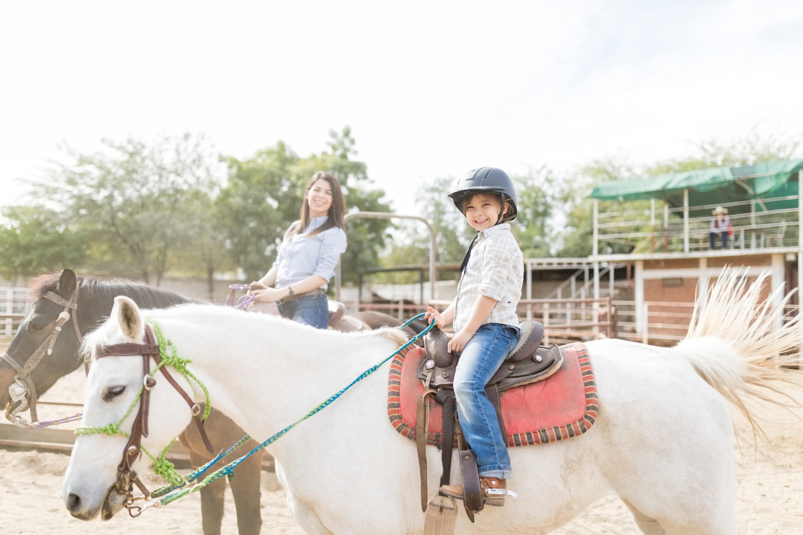 child riding a horse with adult riding horse in background